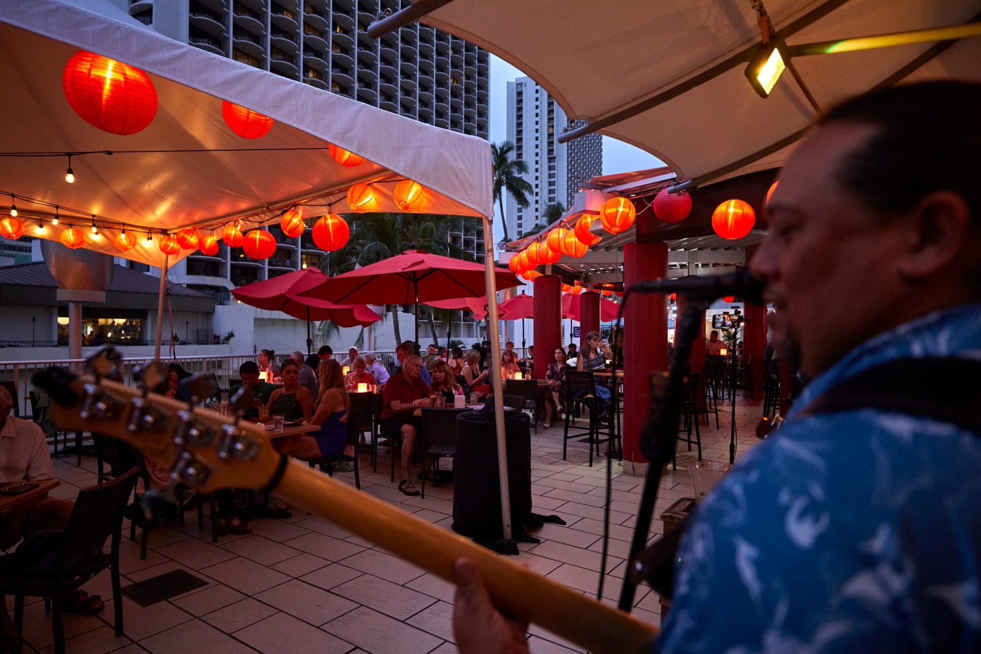 A Hawaiian group playing live music at Tiki's Grill & Bar with a bar and guests in the background, showcasing the restaurant's daily live entertainment.