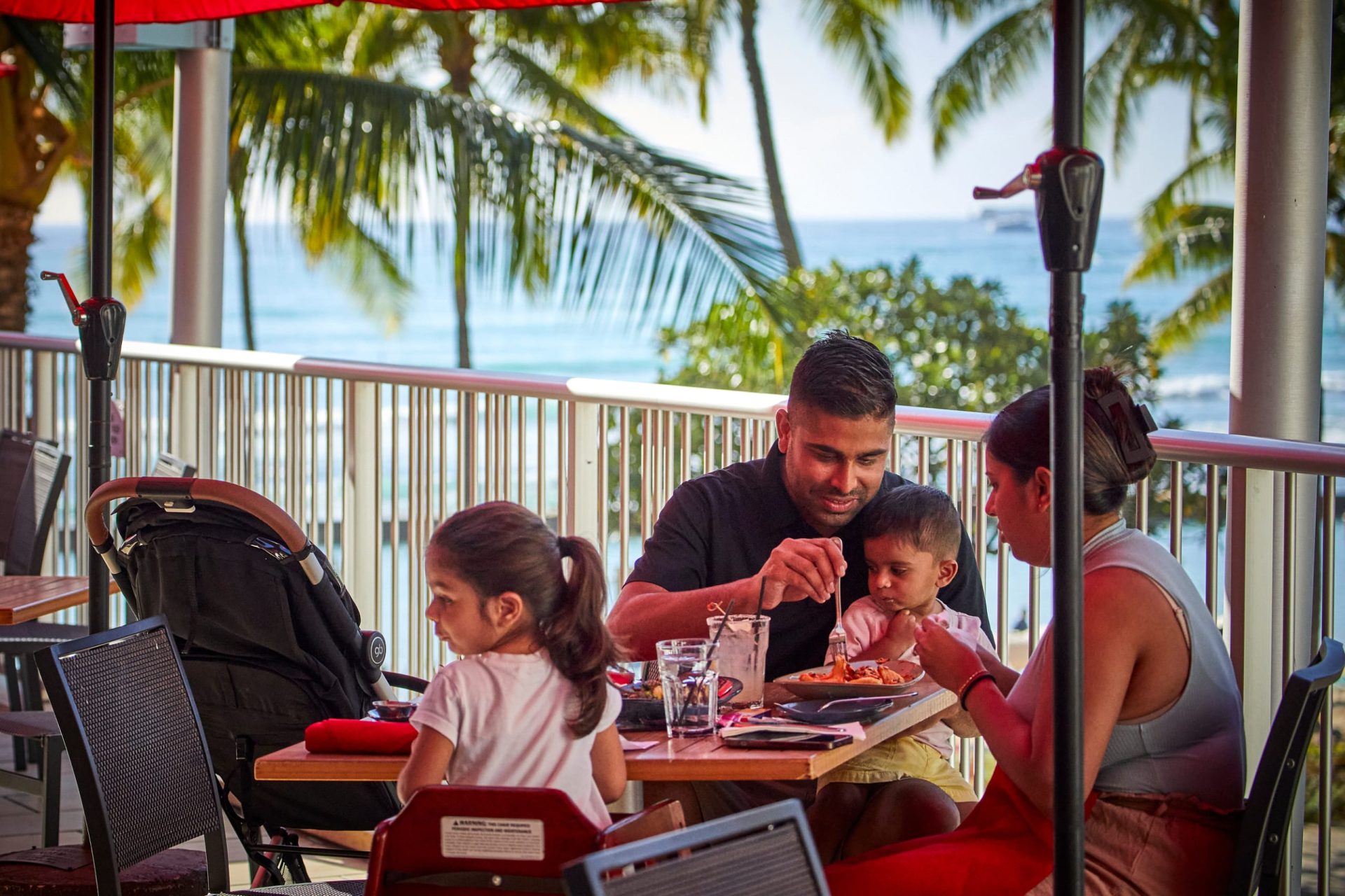 A family with children eating and enjoying the ocean view at an outdoor table at Tiki's Grill & Bar.