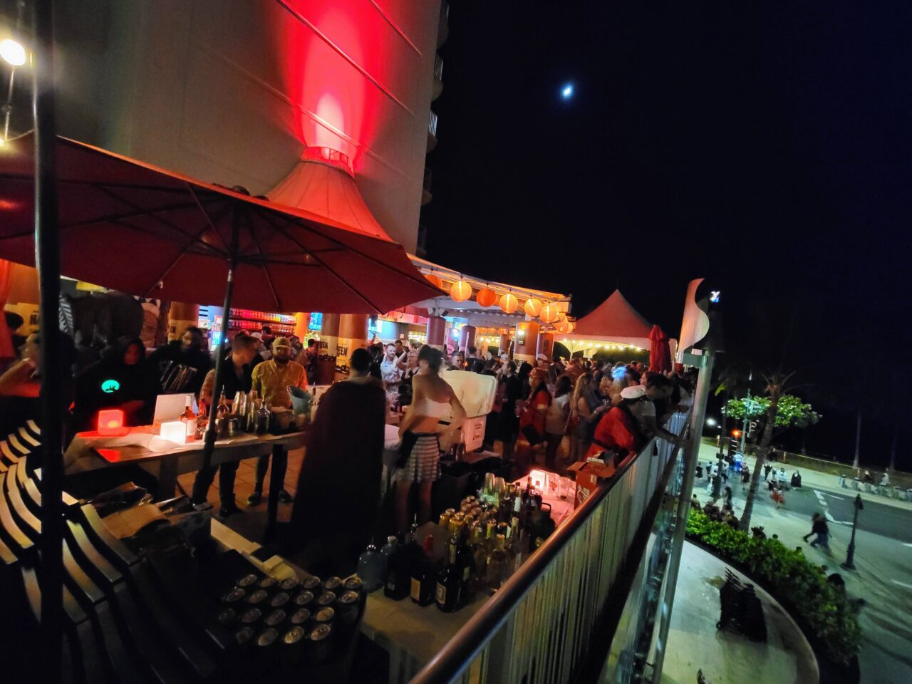 Full outdoor lanai at Tiki’s Grill & Bar glowing with tiki torches and Waikiki Beach views during the Halloween night celebration.
