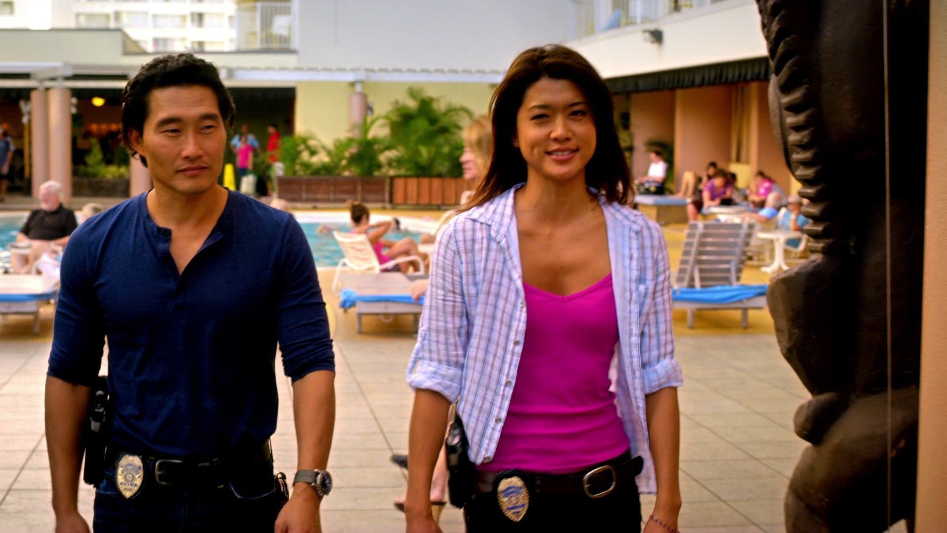 Chin Ho Kelly (Daniel Dae Kim) and Kono Kalakaua (Grace Park) crossing the pool deck into Hina's Lanai beside the large tiki statue during Hawaii Five-0 filming at Tiki's Grill & Bar in Waikiki